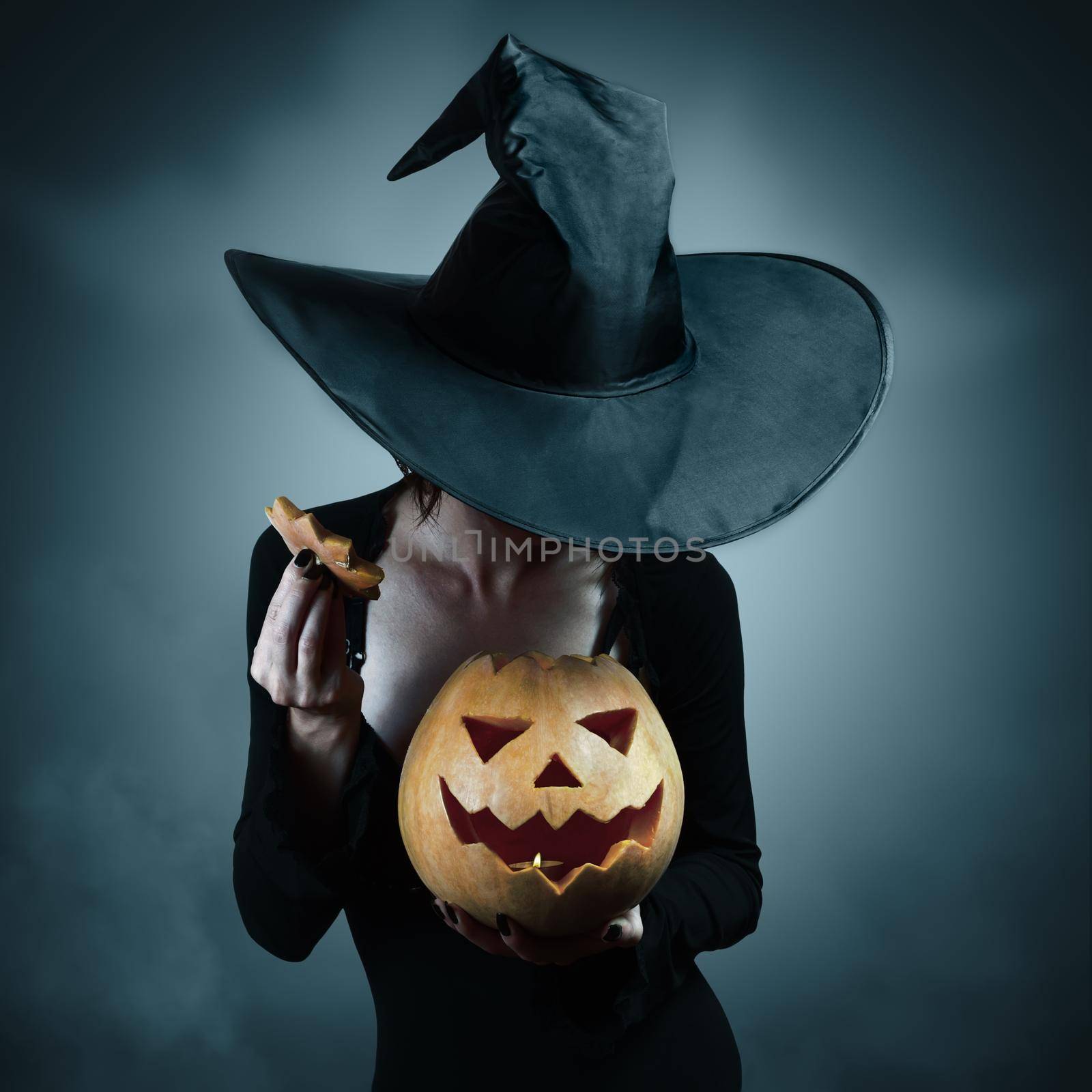 Woman in witch costume opens carved Halloween pumpkin