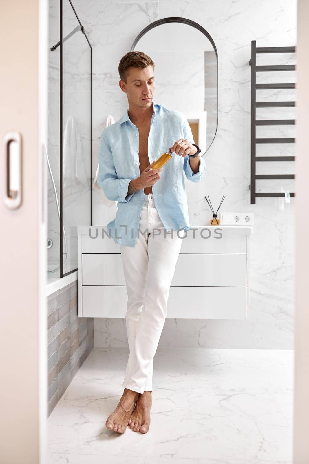 Photo of adult caucasian beautiful man in front of mirror in light modern bathroom by Yaroslav_astakhov