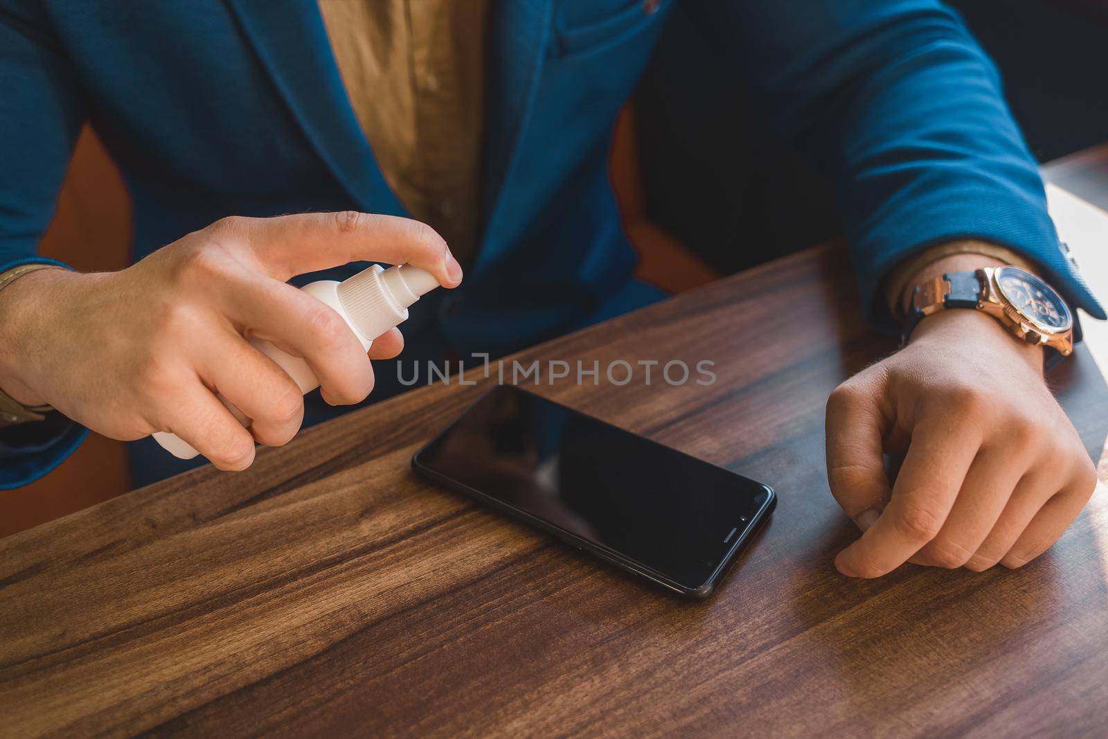 Businessman hands hold antiseptic and spray on phone screen on table background.