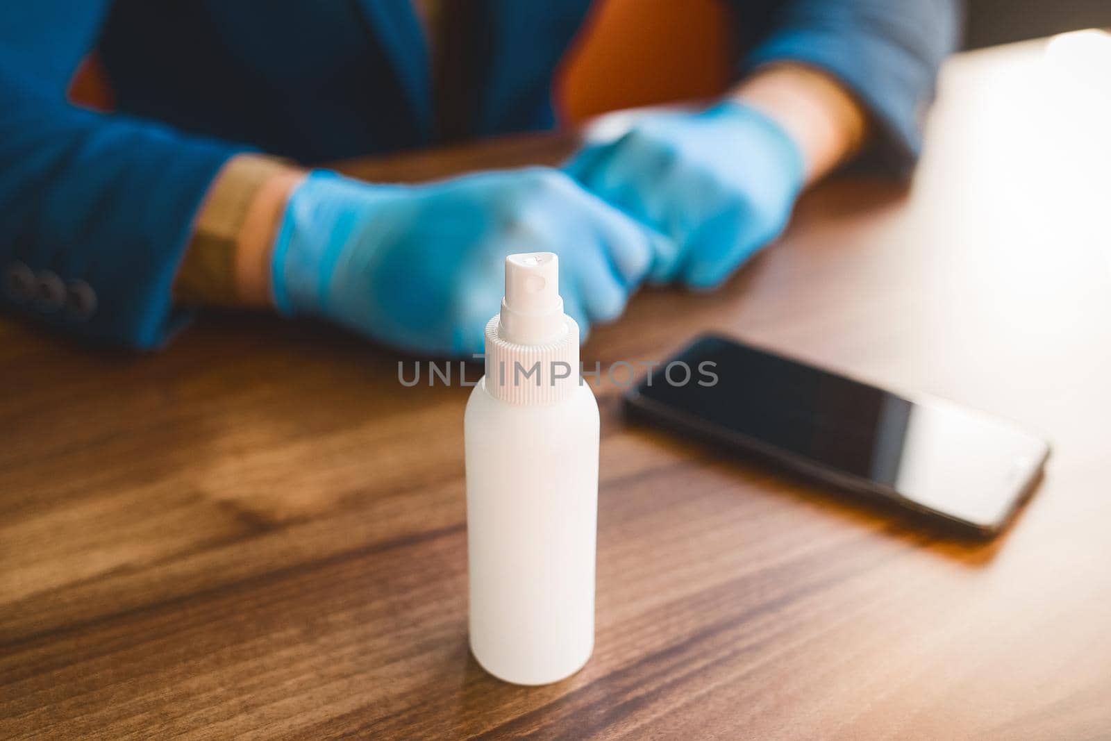 Antiseptic on the background of the hands of a businessman in protective medical gloves and a phone on the table.