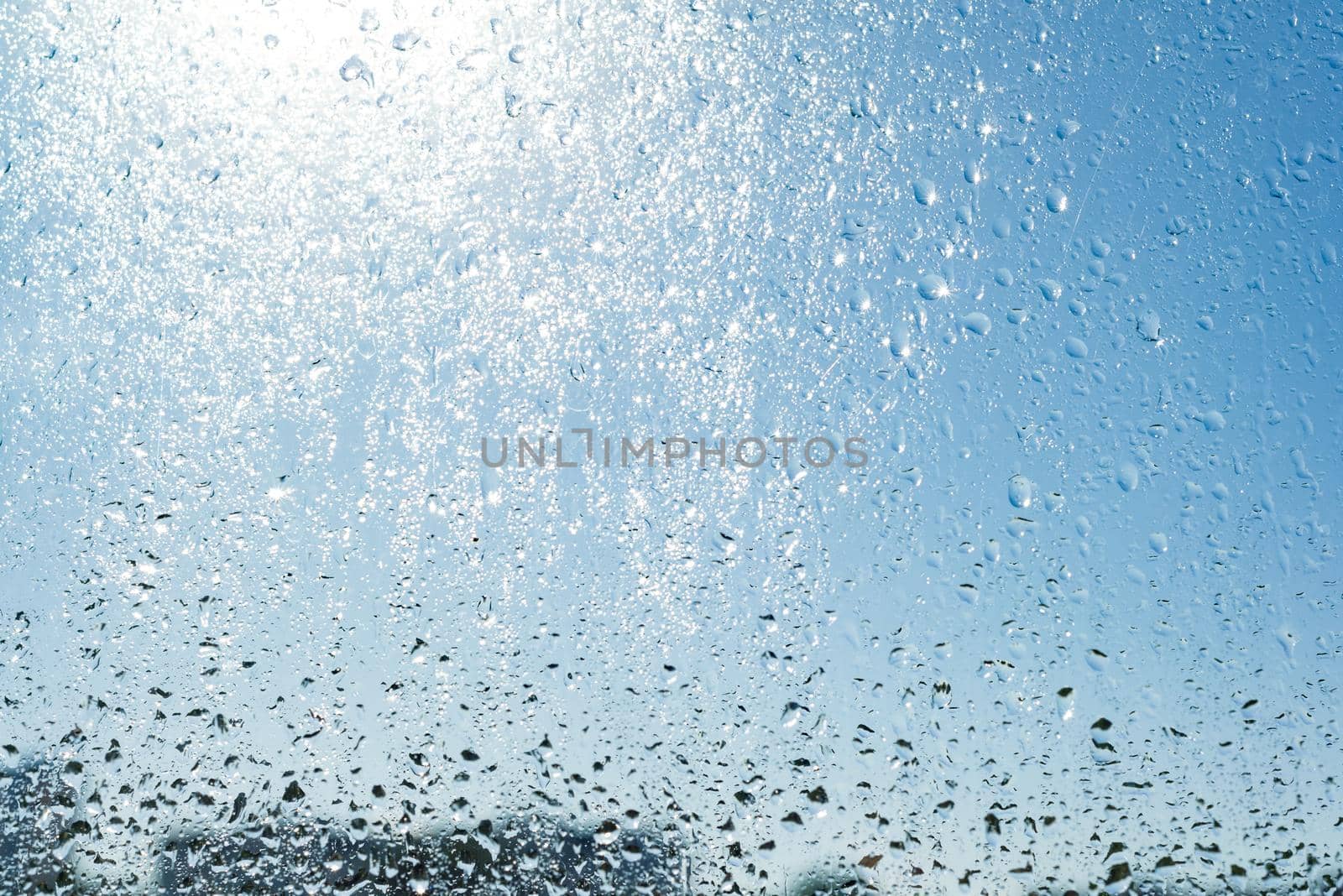 Rain drops on the window. Background blue sunny sky, drops shine in the sun.