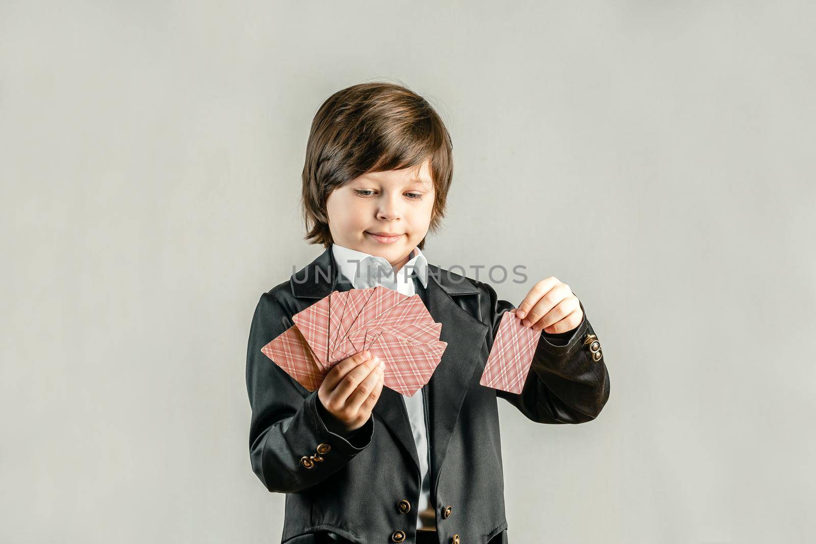 Young six year old boy wearing black suit and showing playing cards trick during illusionist performance. Pocker player