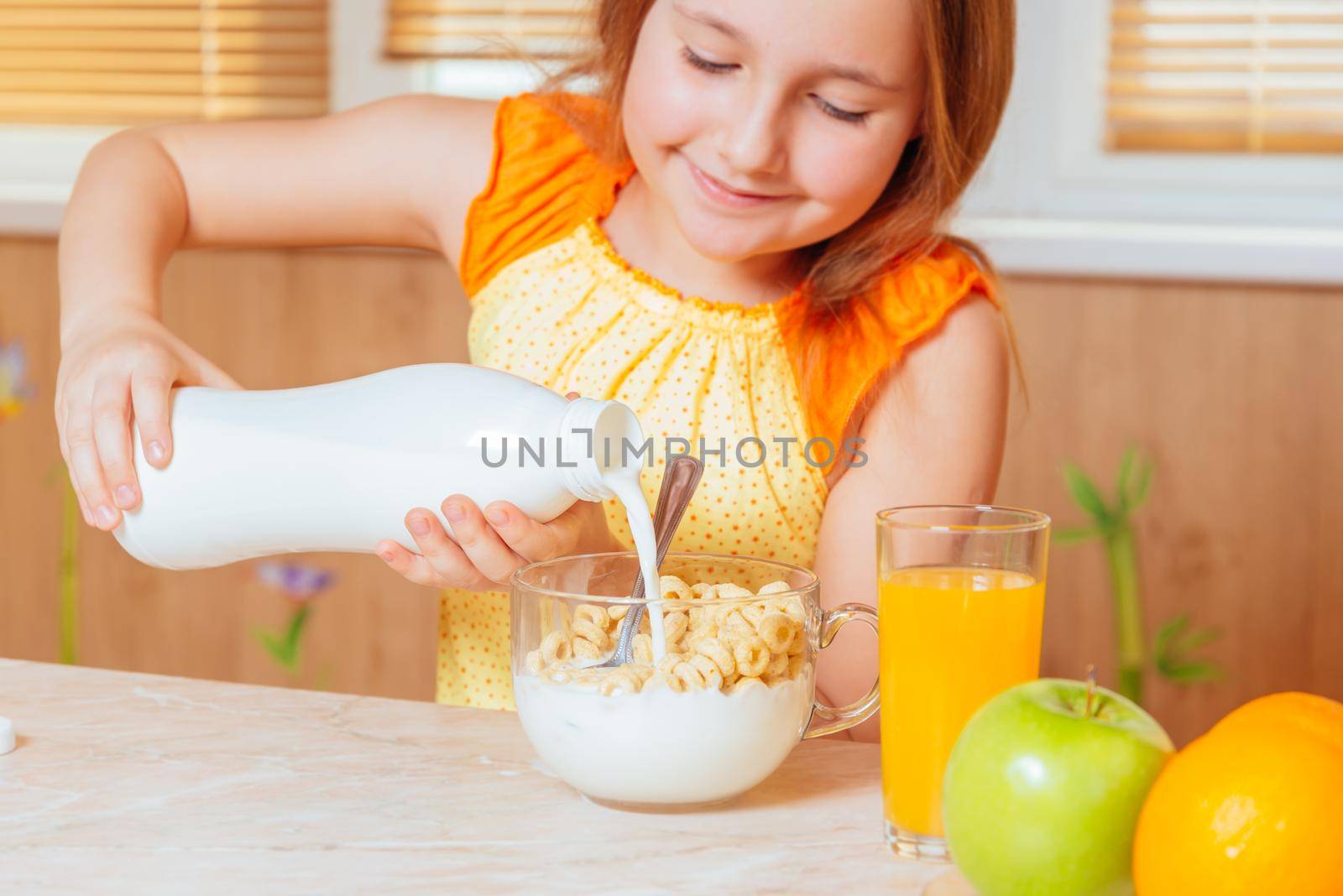 Happy little girl pours milk in cereal flakes for breakfast