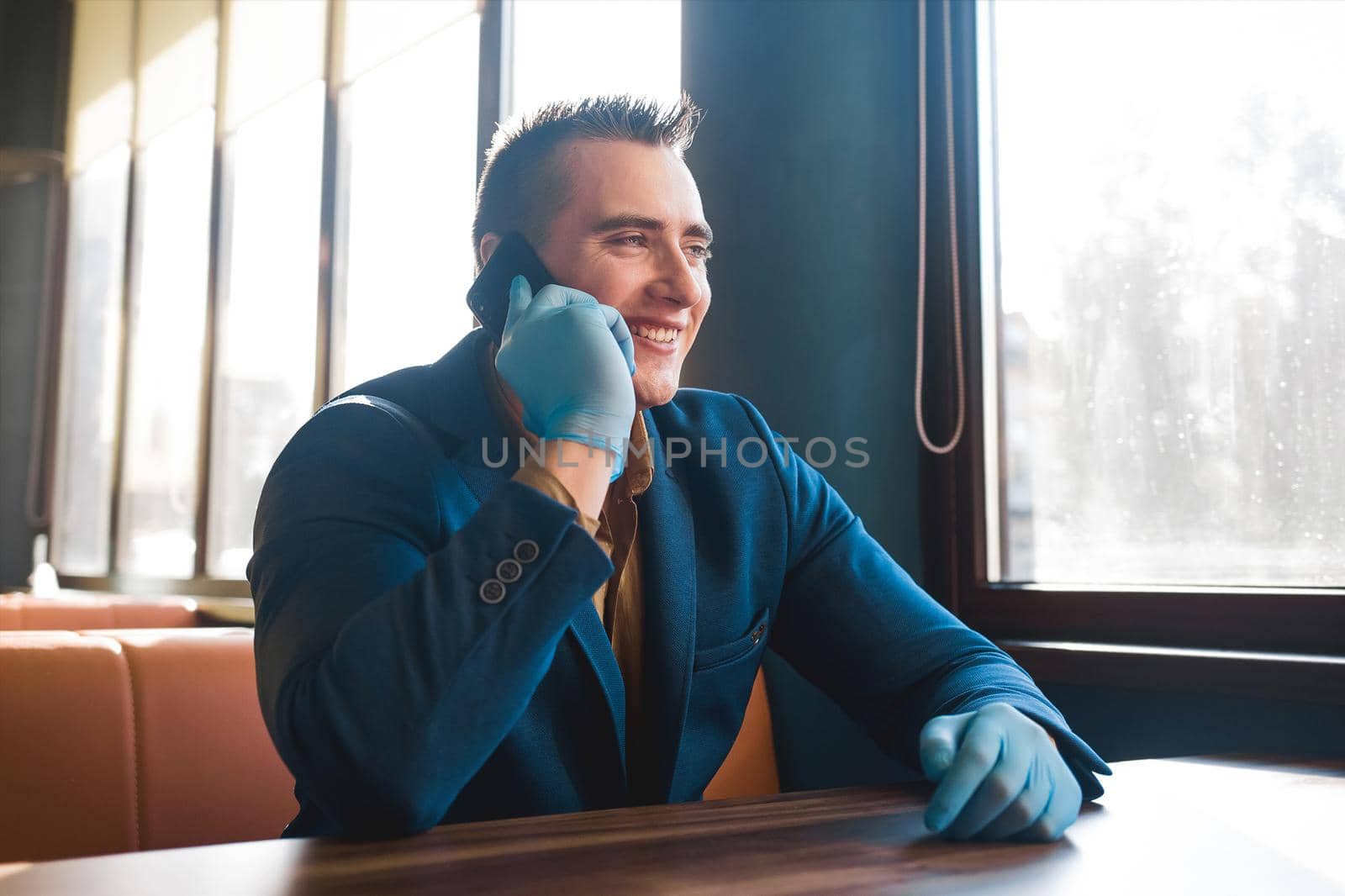 Young european guy businessman in blue suit and protective medical gloves talking on the phone and smiling.