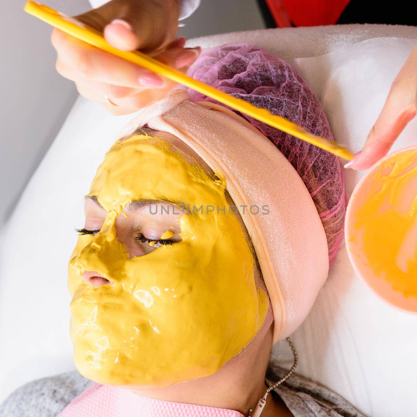 Using a gold mask in cosmetology, a woman at a beautician applying a gold mask on her face. by Niko_Cingaryuk