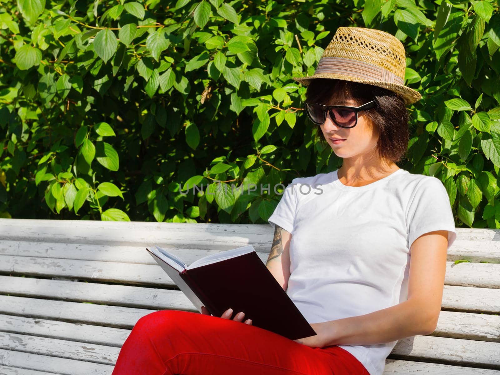 Hipster woman reading a book on a bench in a summer garden, side view