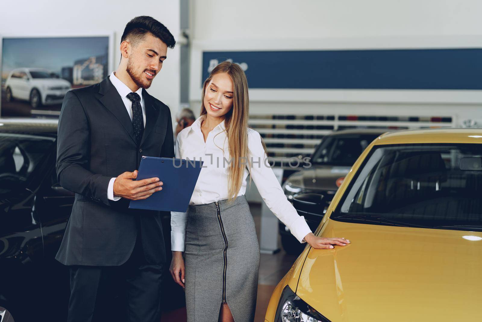 Man car dealer showing a woman buyer a new car in car salon