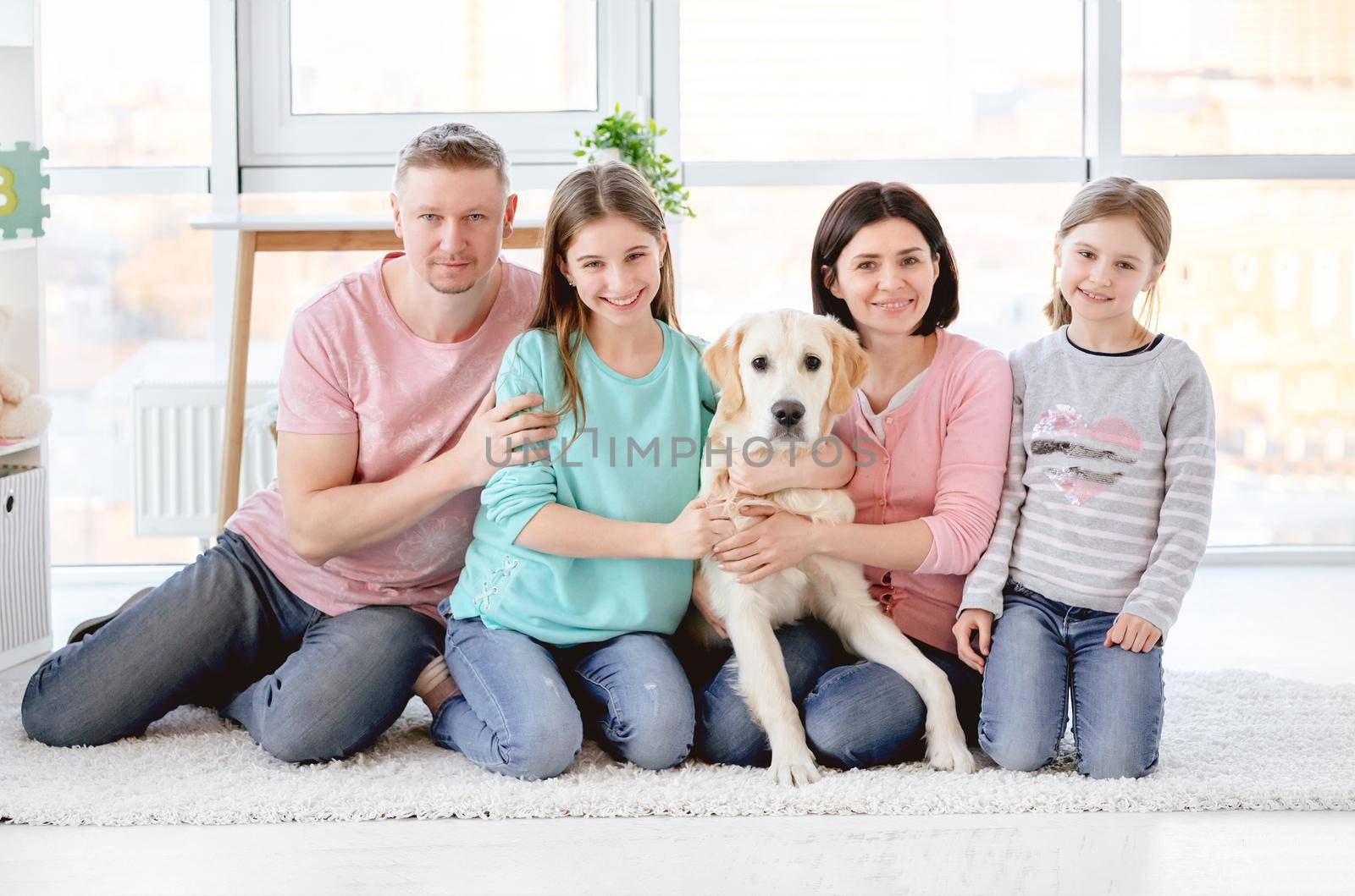 Happy family with dog sitting on floor in light room