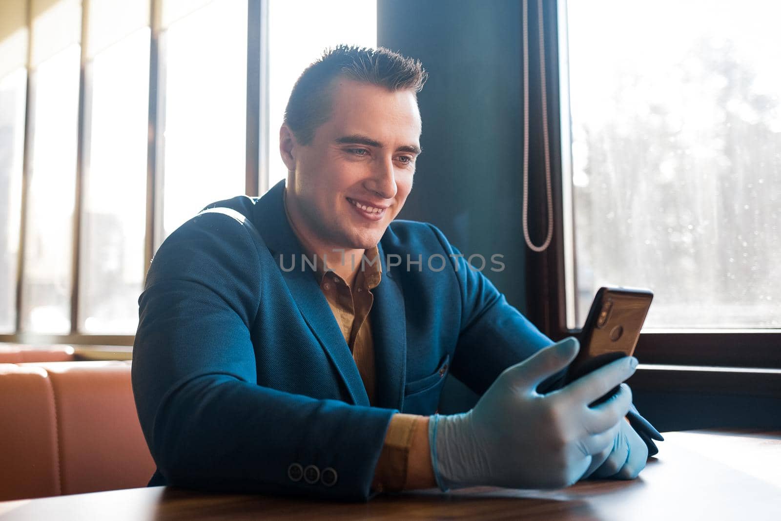 Young caucasian guy businessman in a blue suit and protective gloves looks into the phone and smiles.