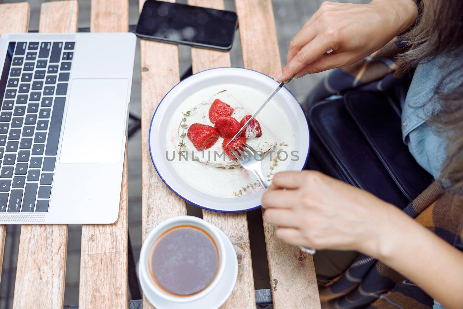 Senior woman eats delicious toast with strawberries and cream near laptop at table outdoors by Yaroslav_astakhov