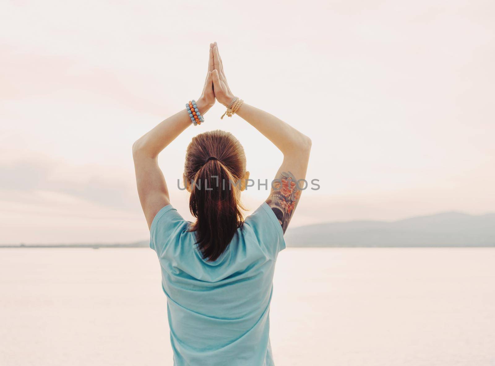 Young woman doing yoga and meditating on background of sea, hands in praying gesture.