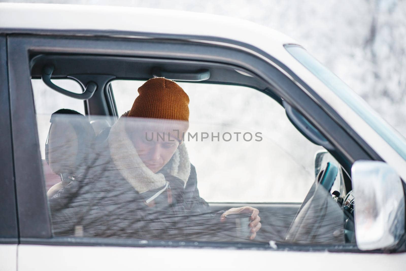 Traveler young man sitting with cup of hot drink in car in winter.