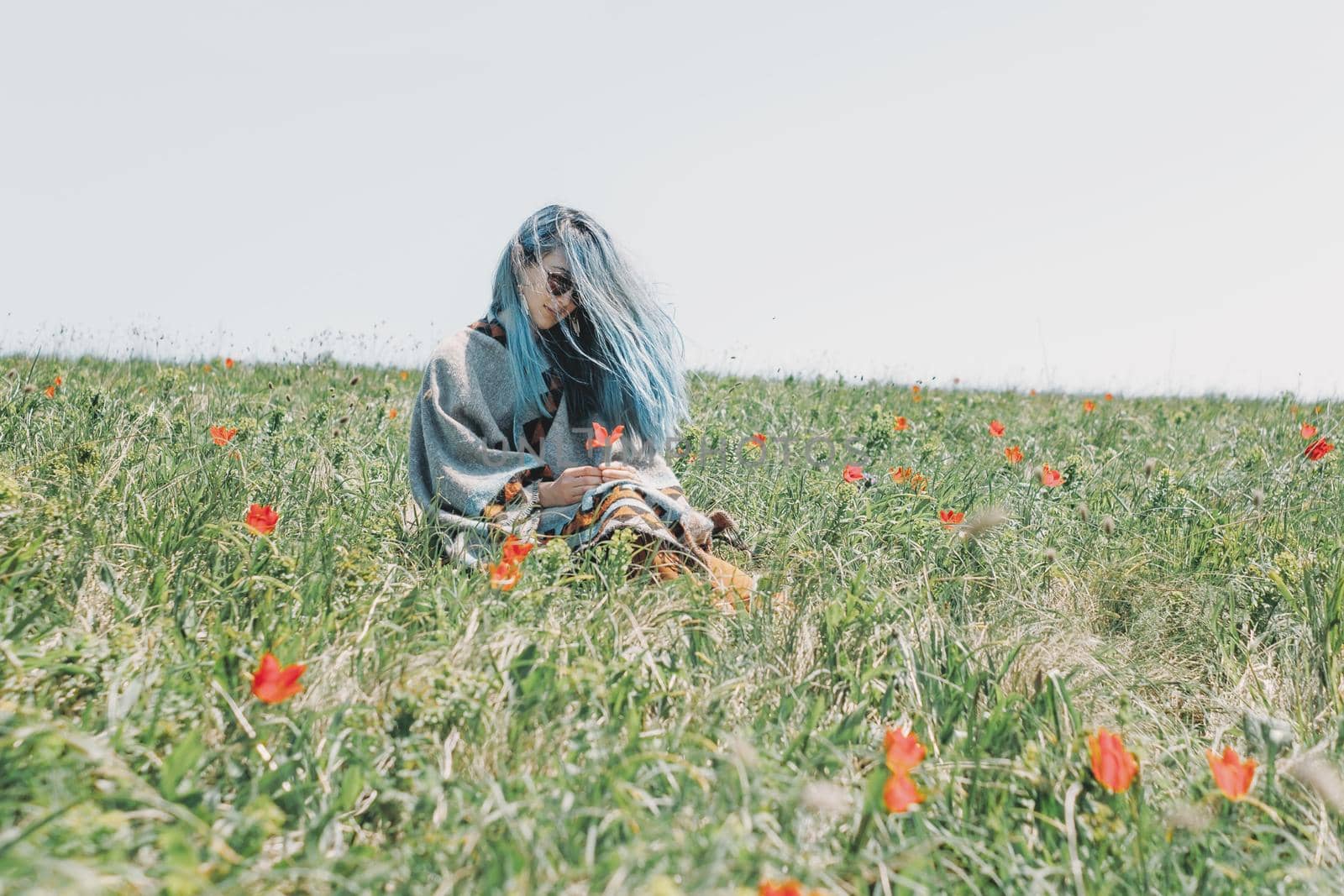 Beautiful young woman with blue hair rests on red tulips meadow.