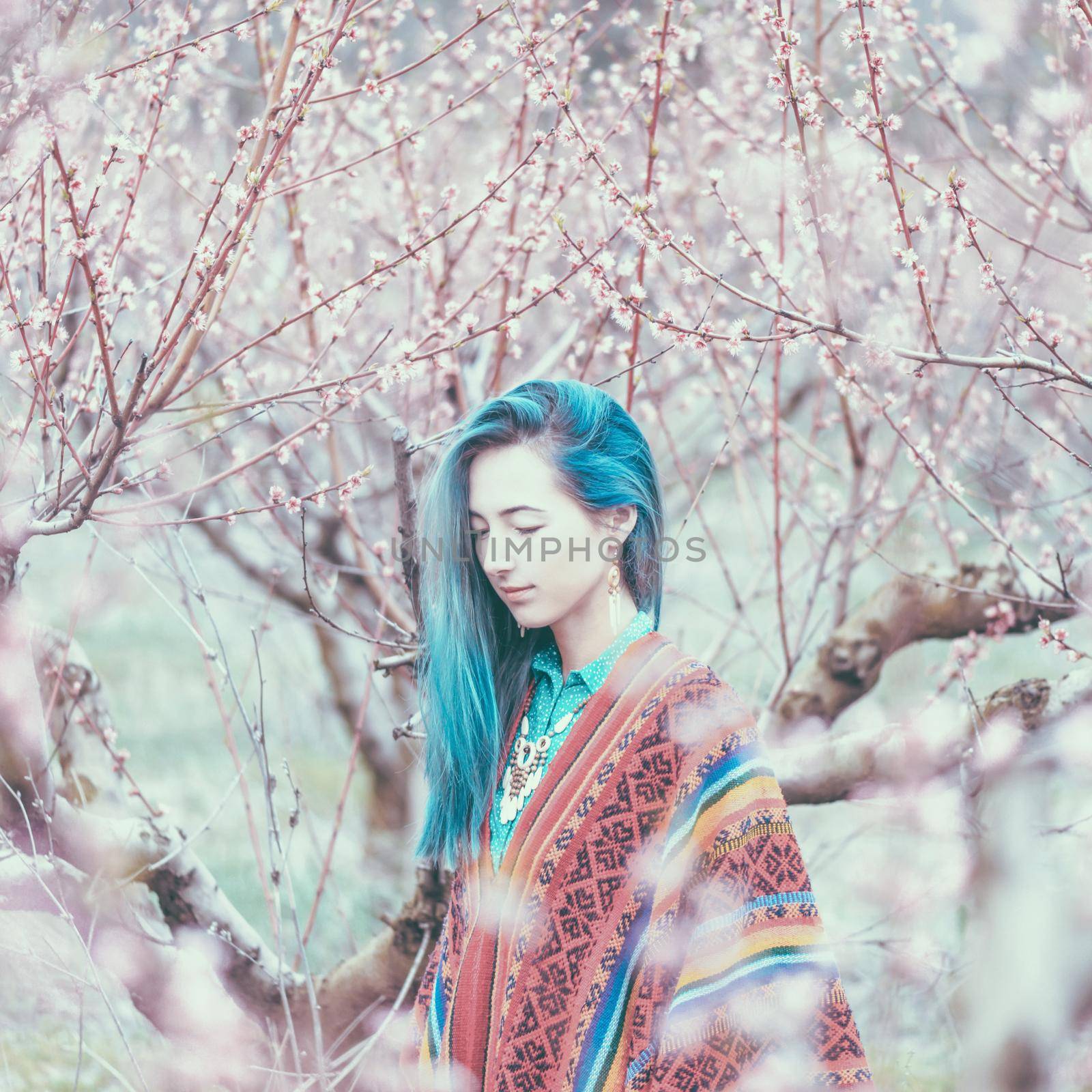 Boho style beautiful girl with blue hair walking in blossoming tree garden. Toned image.