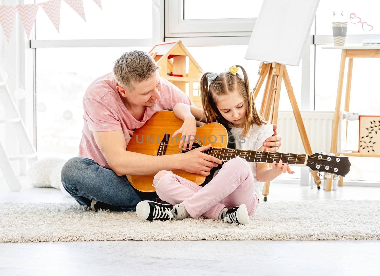 Good father teaching cute little daughter to play guitar in light room