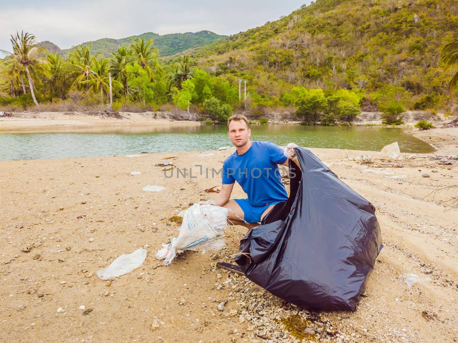 Man in gloves pick up plastic bags that pollute sea. Problem of spilled rubbish trash garbage on the beach sand caused by man-made pollution and environmental, campaign to clean volunteer in concept.