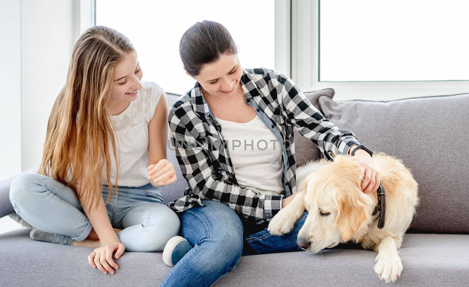 Happy daughter and mother sitting on sofa next to lovely dog