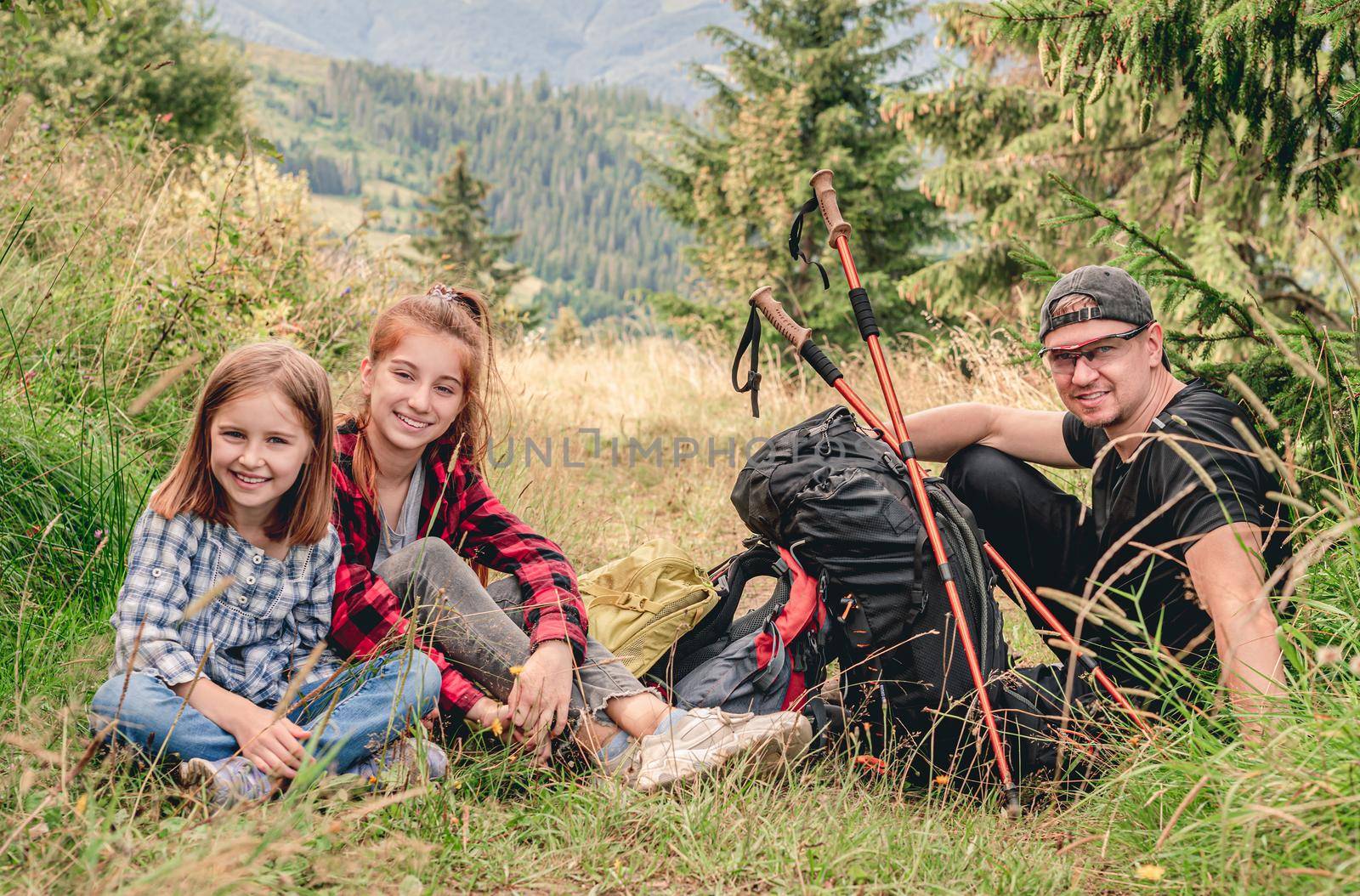 Smiling sisters with father resting during mountain hiking