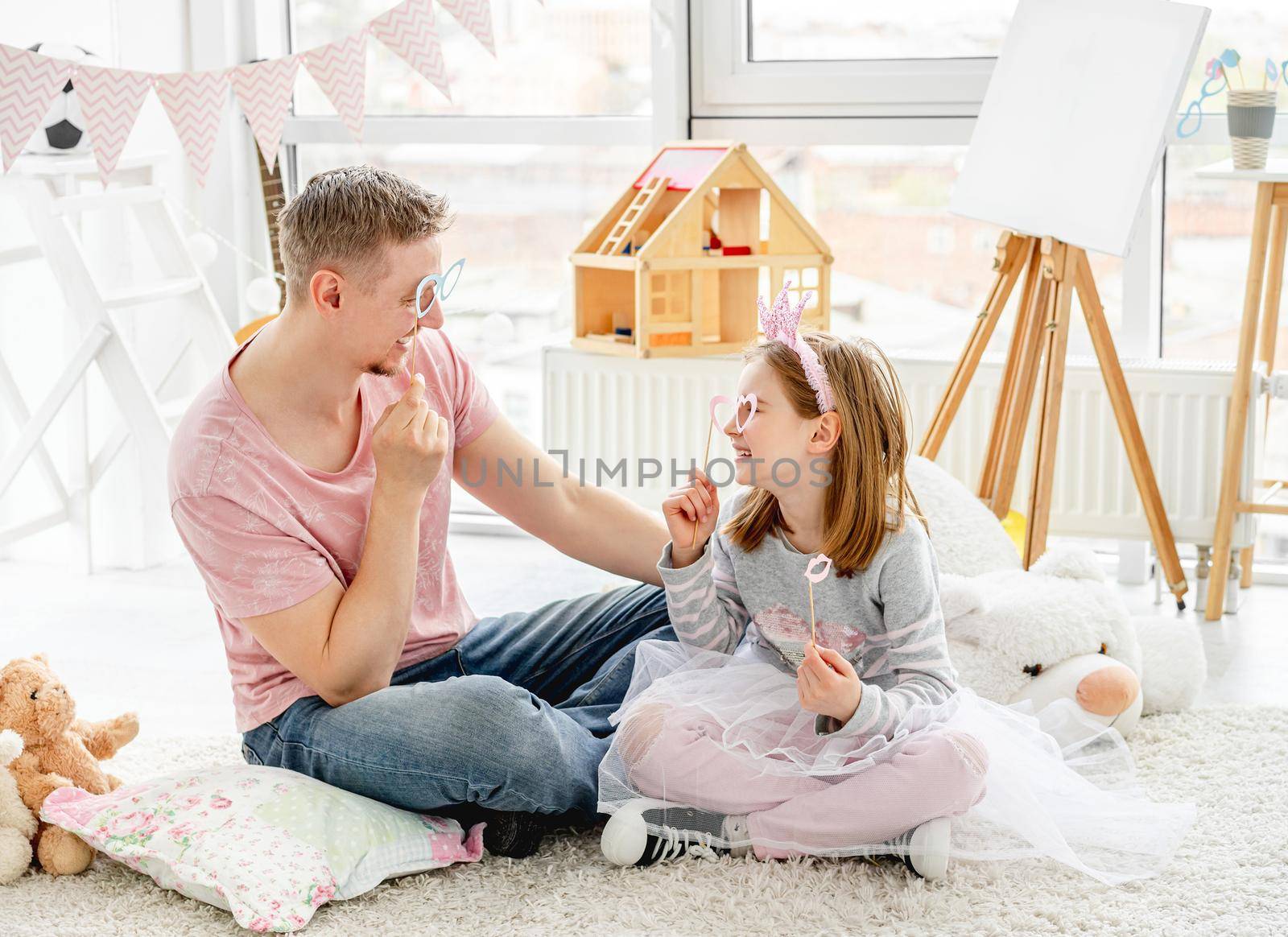 Smiling man and happy girl fooling with glasses on stick indoors