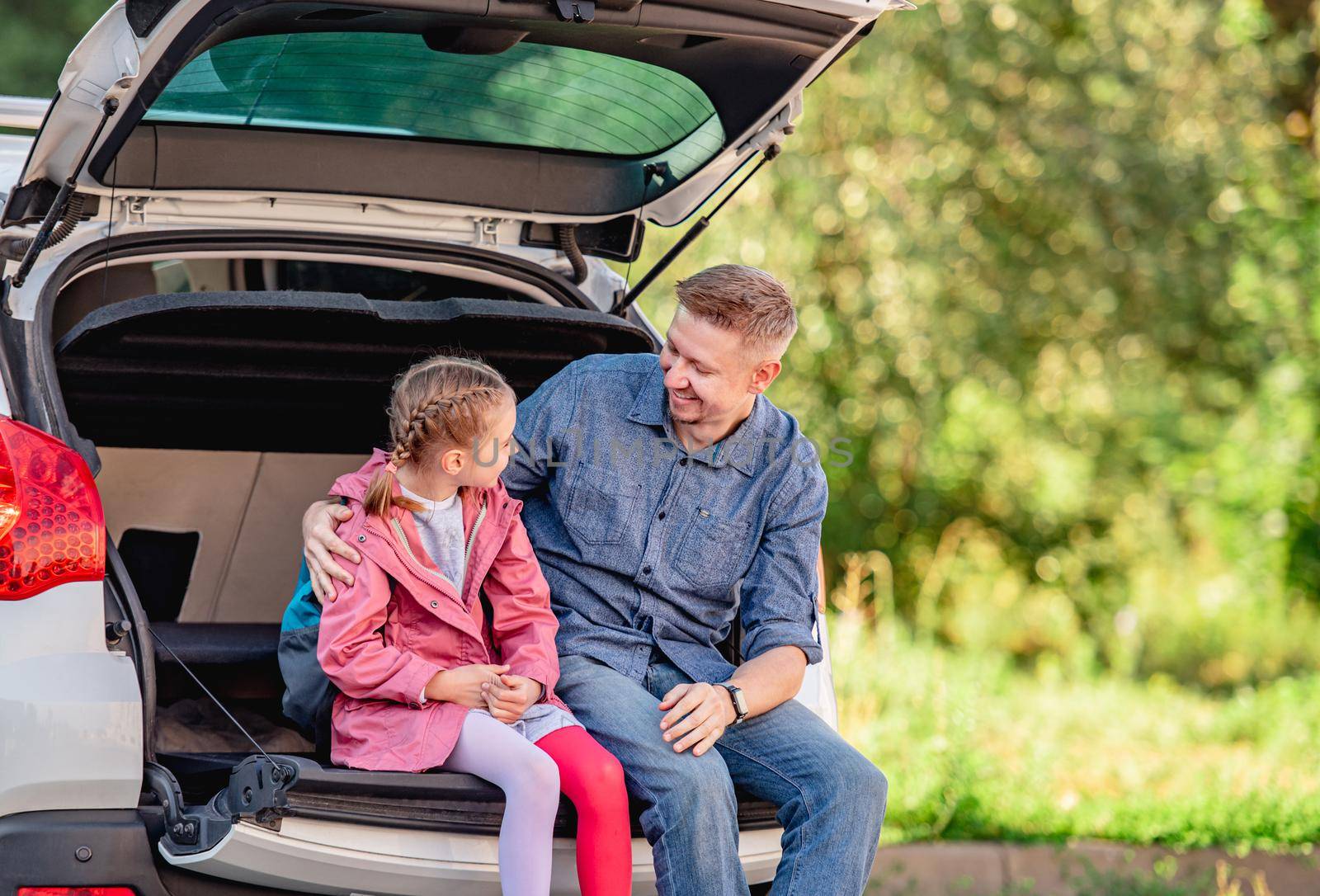 Father with daughter sitting on car trunk after schooling