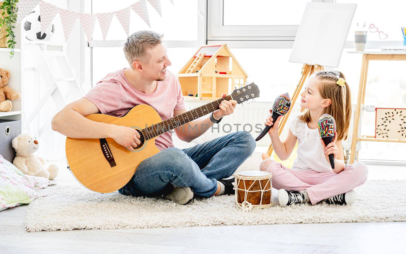Smiling father and little daughter playing musical instruments in kids room
