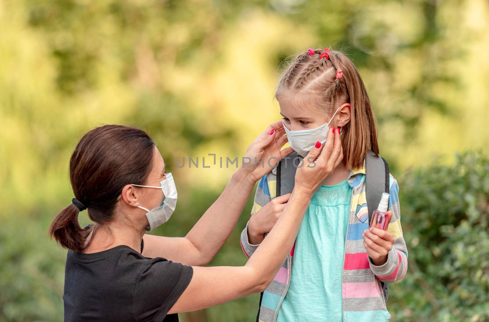 Mother putting protective mask on little daughter before going back to school