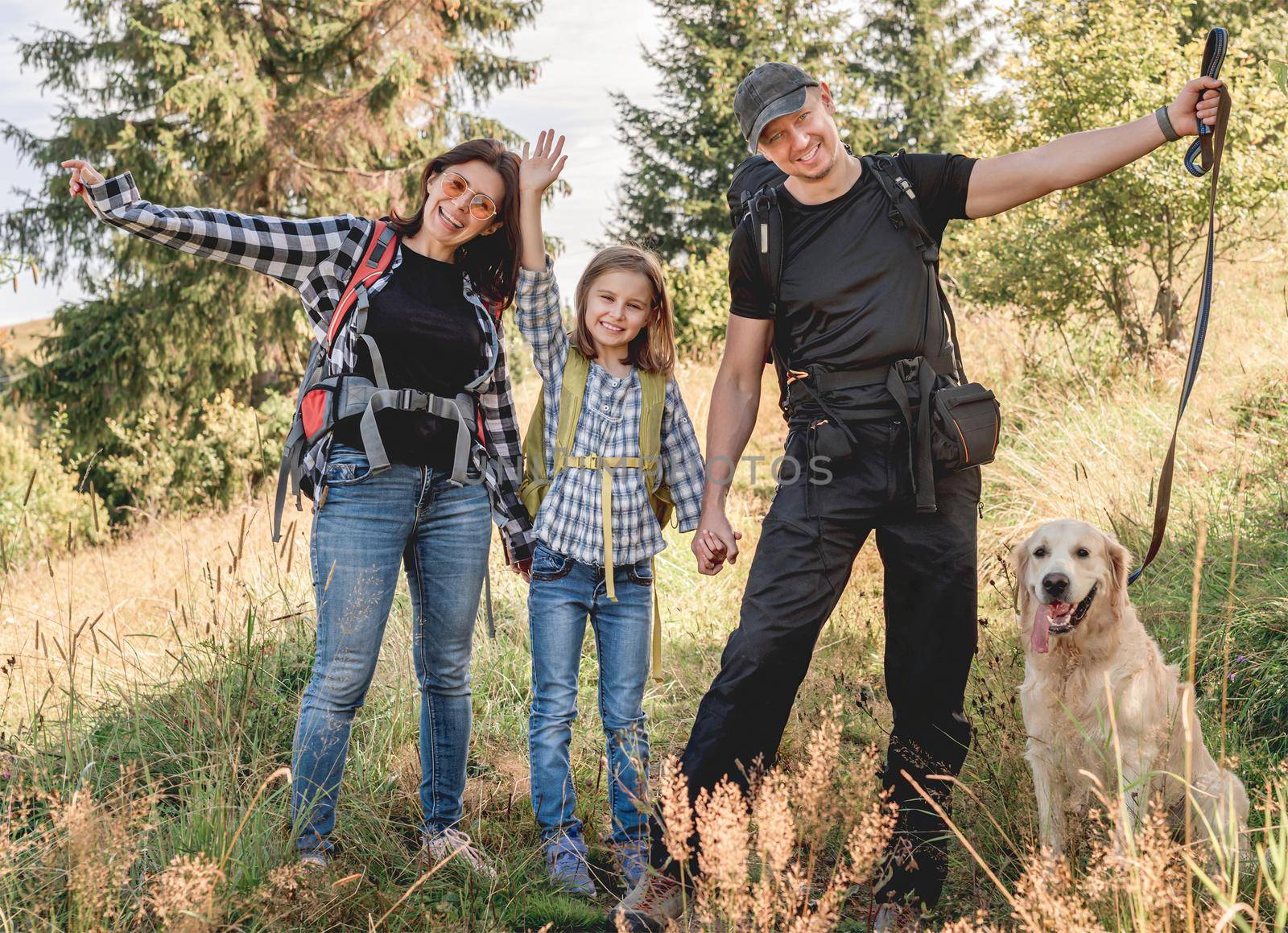 Happy family trekking in sunny mountains with dog in summer