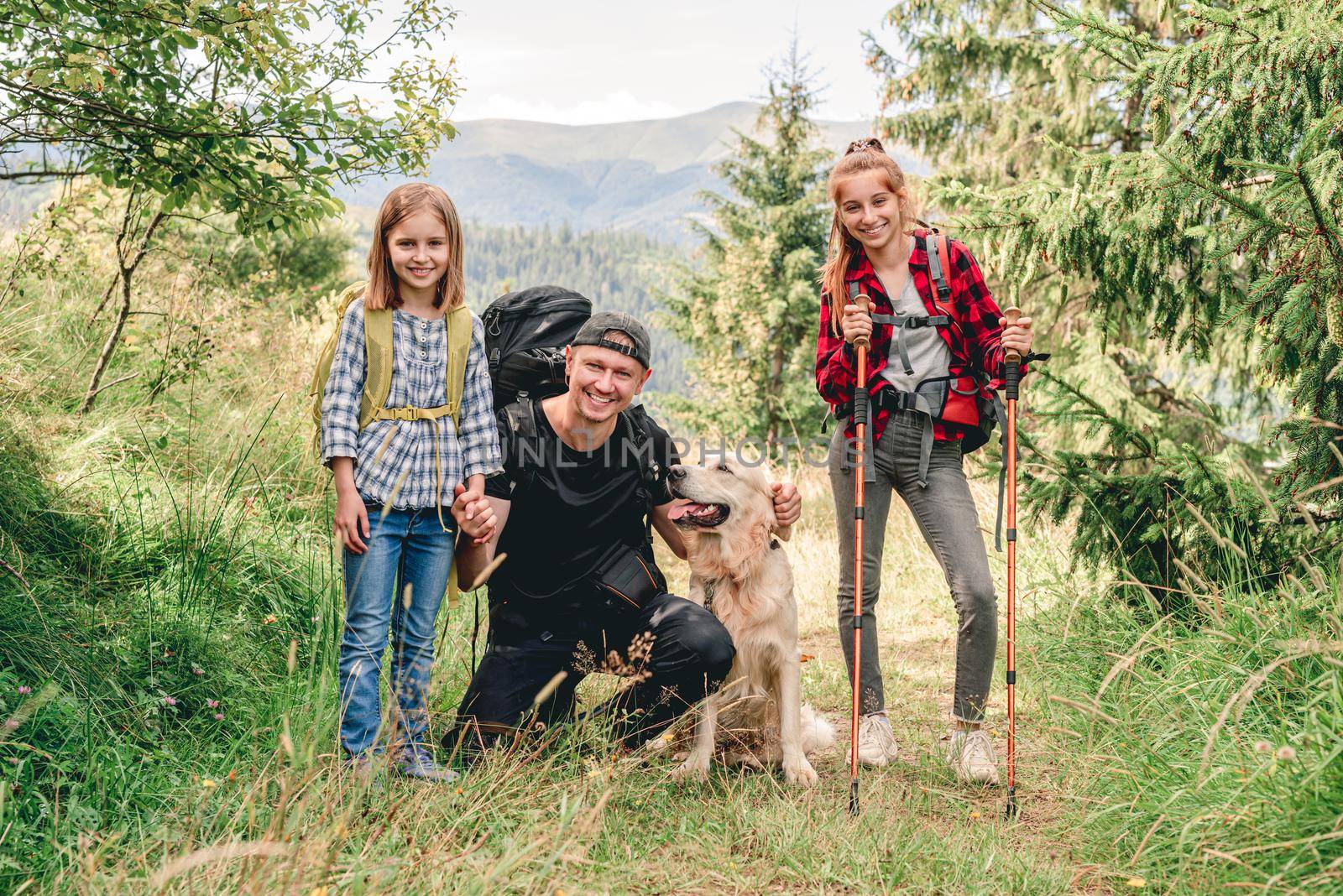 Smiling father with daughters and dog hiking sunny mountain