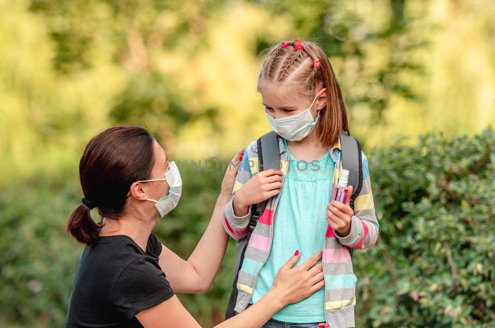 Mother putting protective mask on little daughter before going back to school