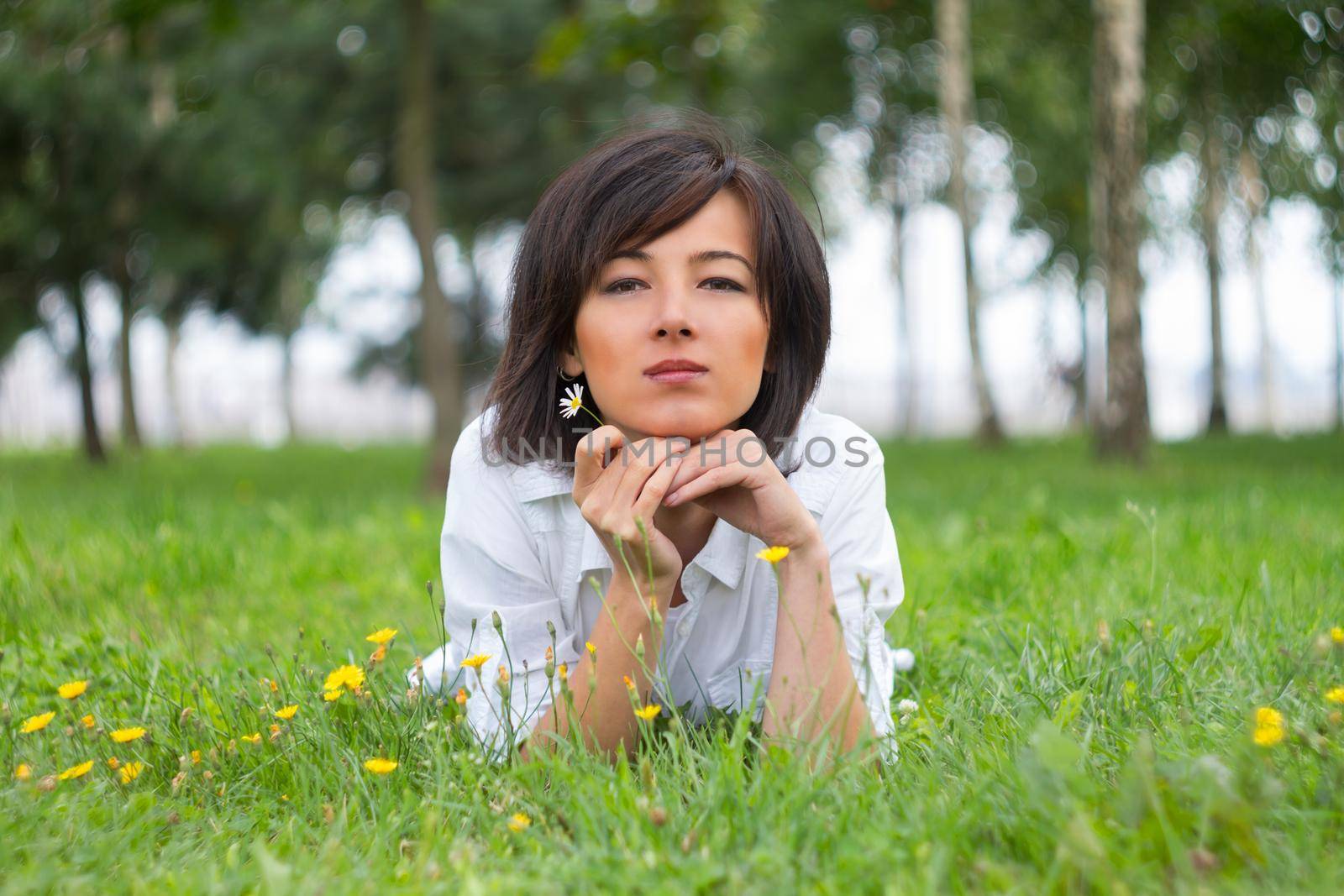 Young woman lying on a meadow with daisy in a summer park