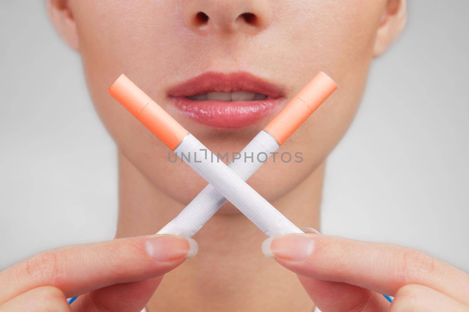 Woman holds two crossed cigarettes in front of her lips