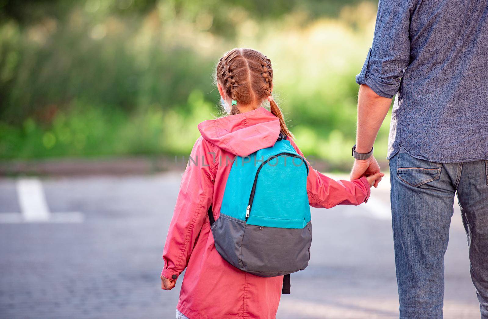 Rear view of little girl with backpack holding father's hand