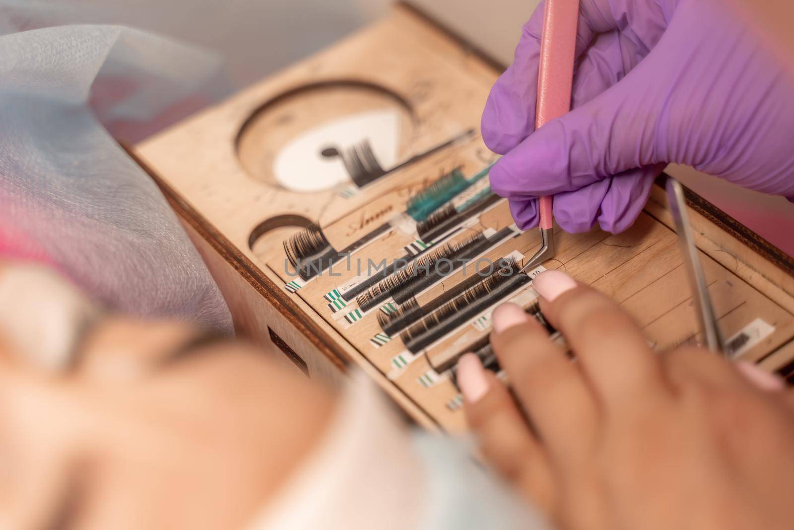 Eyelash extensions, lashmaker tools. Artificial eyelashes on a white tablet and pink silicone brush comb, close up