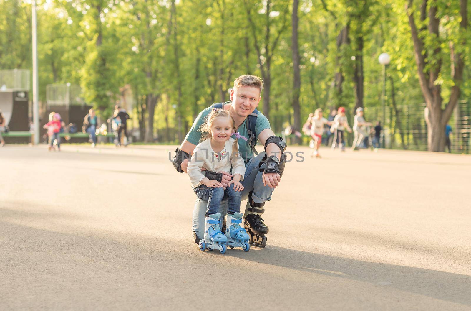 Sibling little girl and her father posing and roller skating in protective form together on weekend