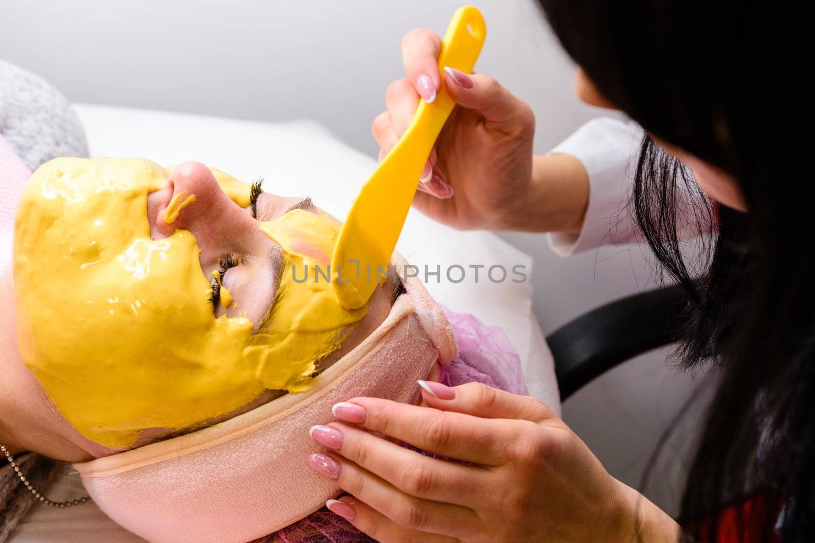 Woman at the beautician applying a relaxing golden mask on the face, restoring and moisturizing the skin. by Niko_Cingaryuk