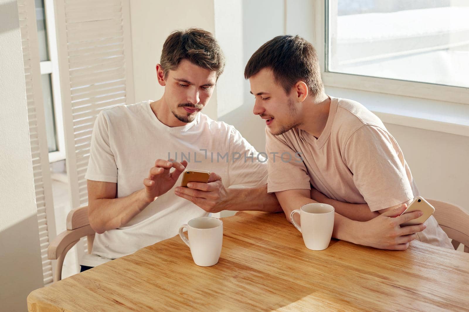 Man hand holding a smartphone and man pointing at it. Two sit at table and work at home