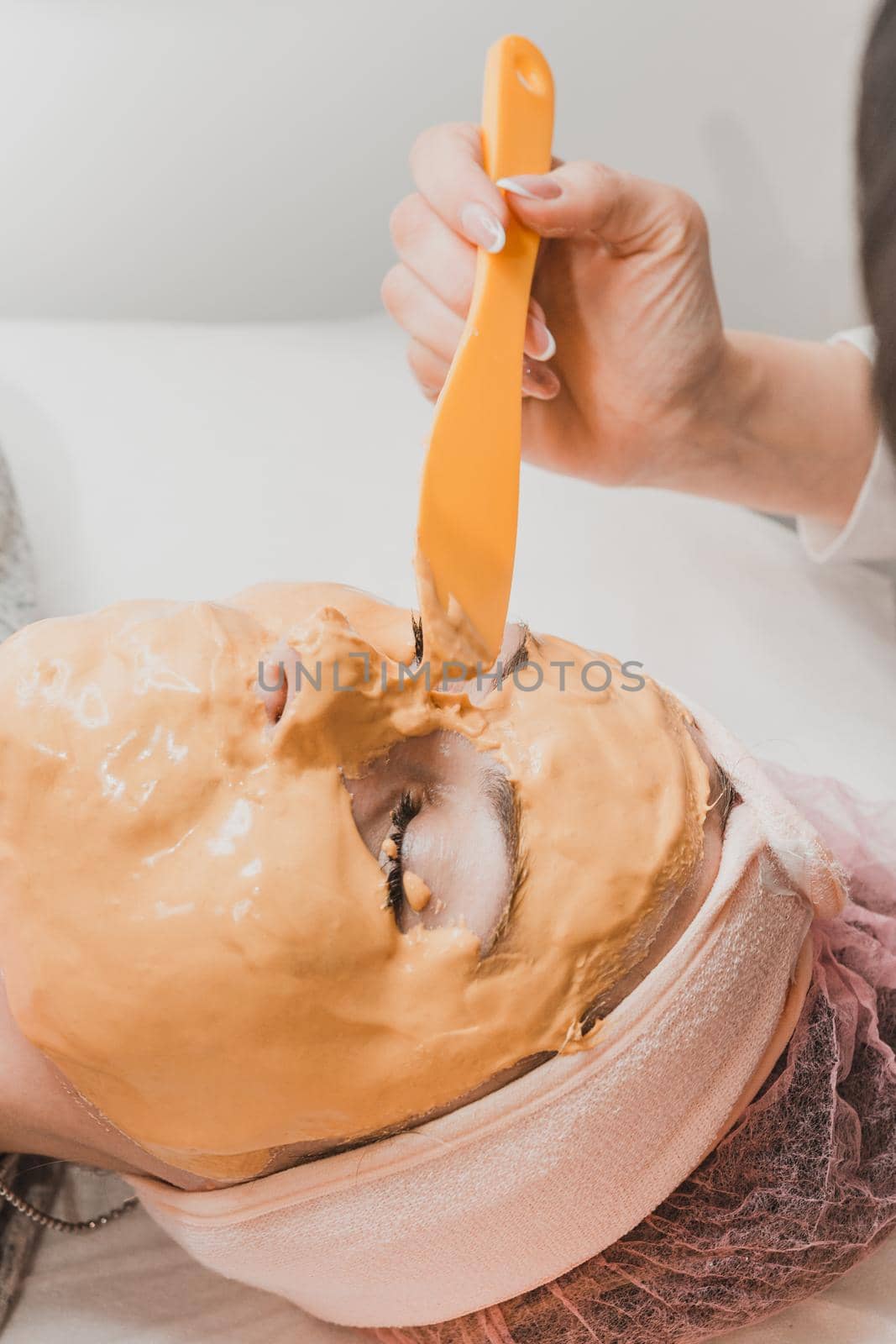 spa treatments in a beauty salon, hand of a professional beautician applying a gold mask on the client's face. new