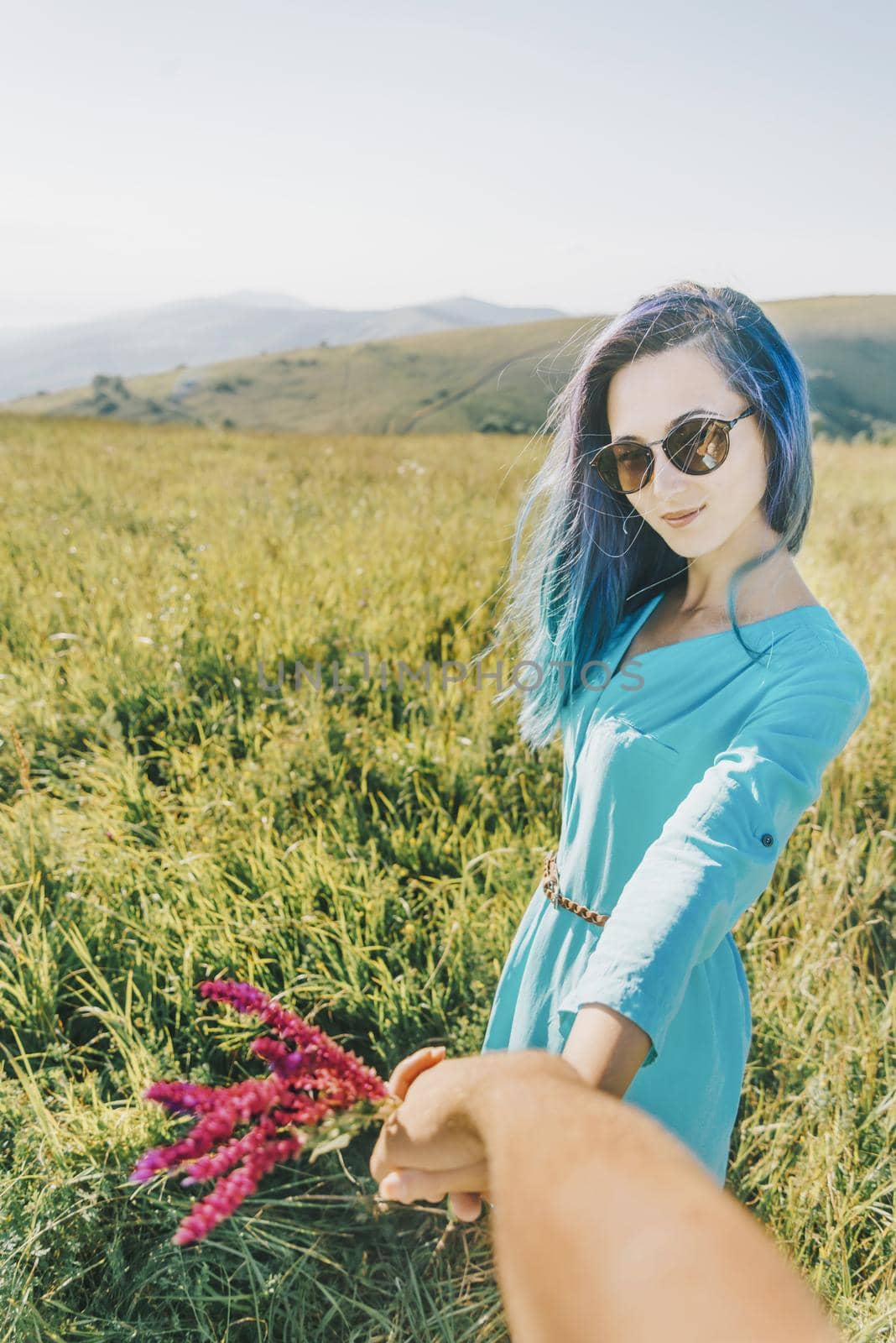 Couple in love. Beautiful young woman holding man's hand and leading him on summer meadow. Point of view shot.