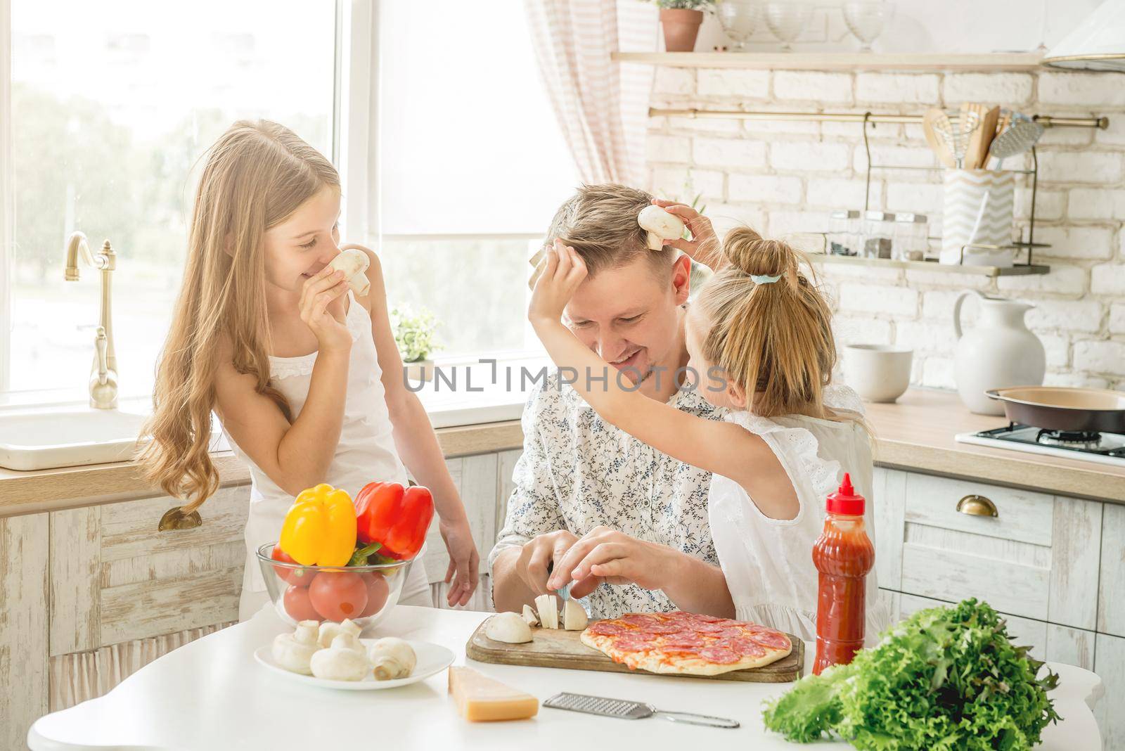 Dad with two small daughters preparing pizza with mushrooms in the kitchen