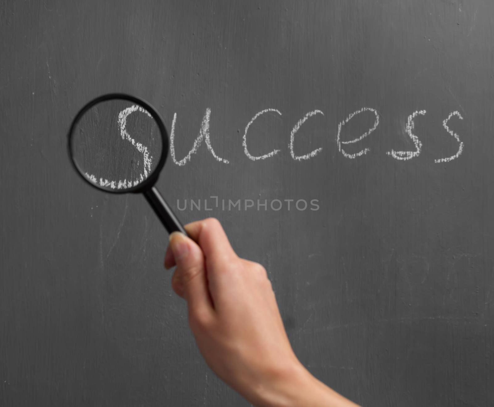 Human hand with a magnifying glass indicates on the word "success"