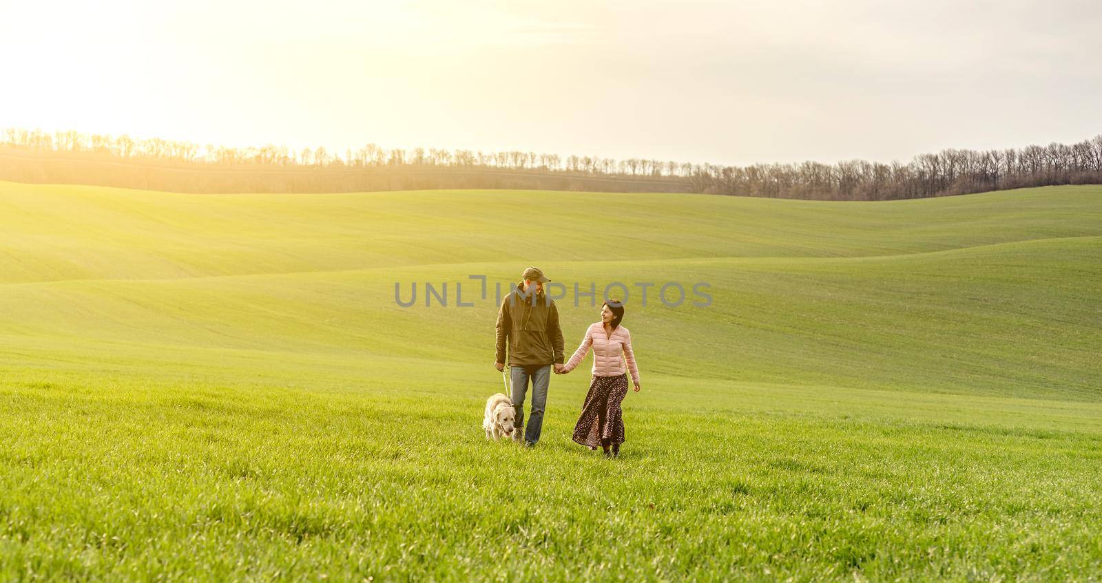 Lovely couple walking cute dog on spring field