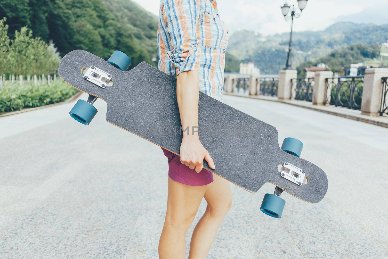 Unrecognizable teenager standing with longboard outdoor.