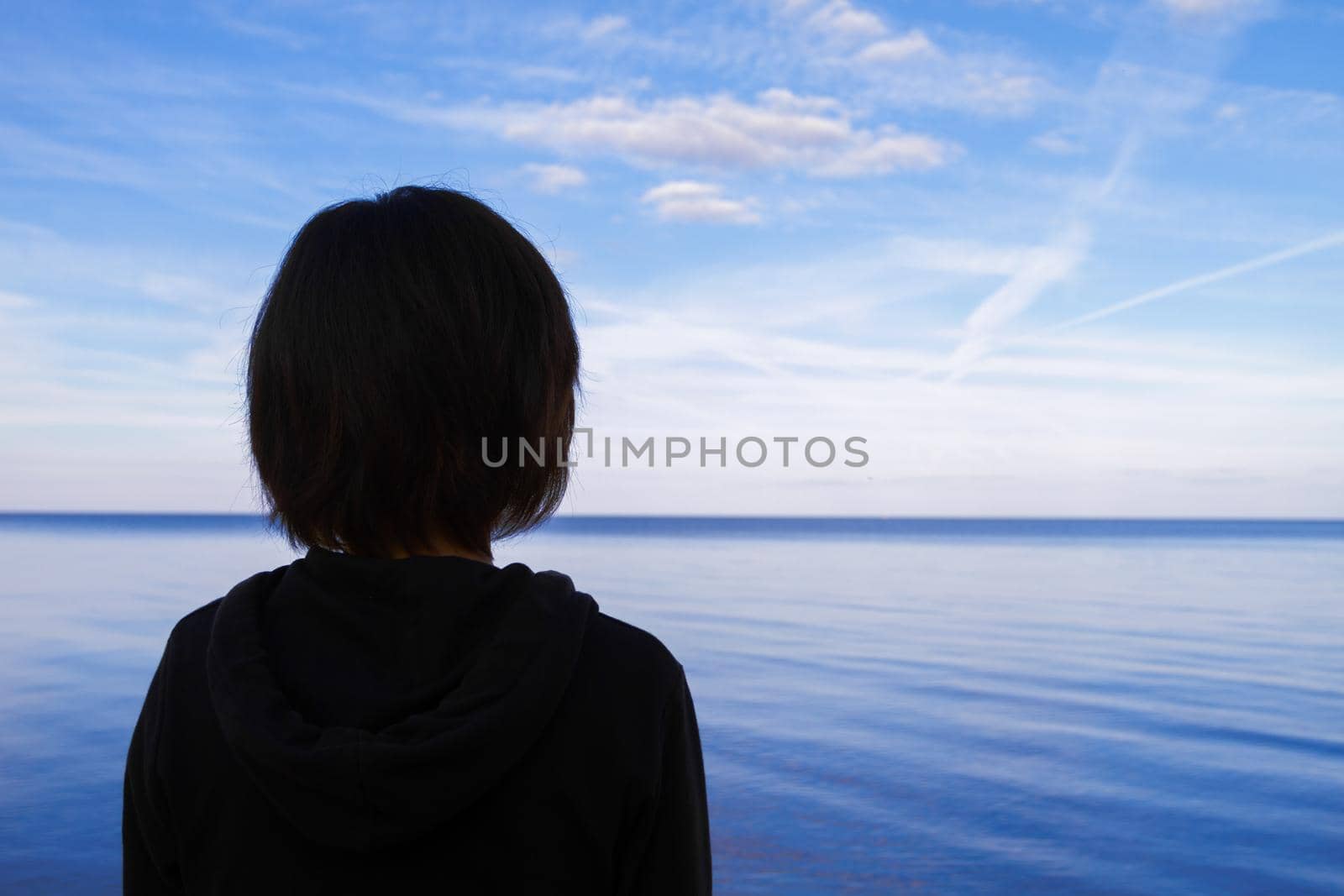 Young woman admires the lake, thinking about life, view from the back