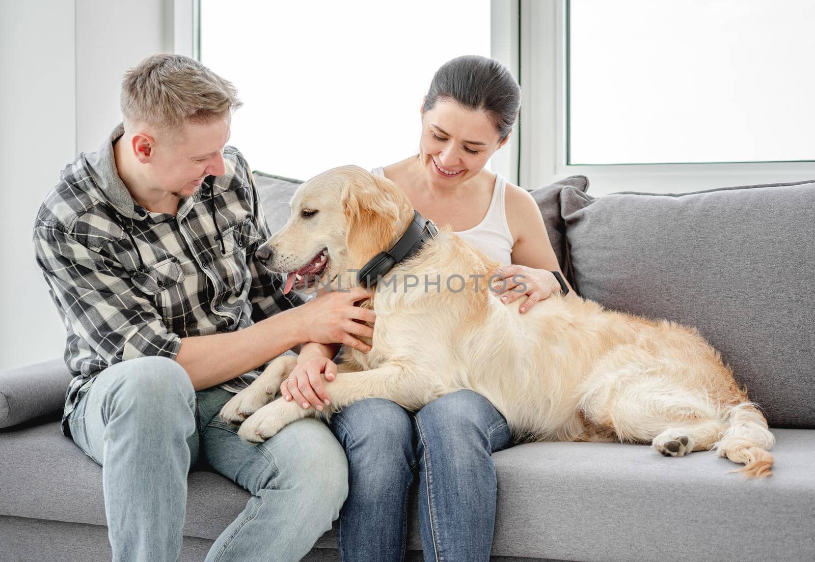 Beautiful woman and man cuddling cute dog in light room
