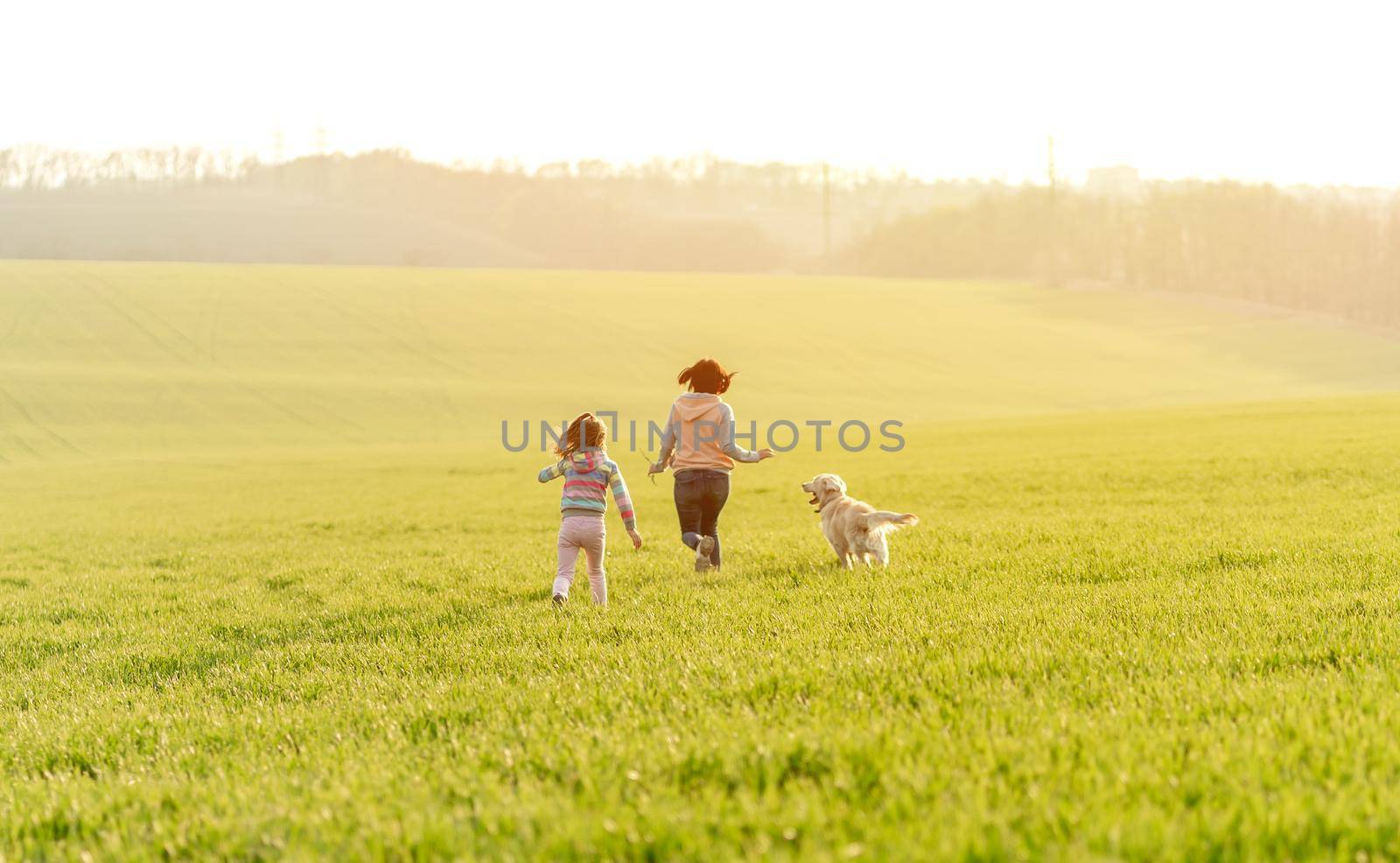 Mother and daughter having fun with dog on spring field