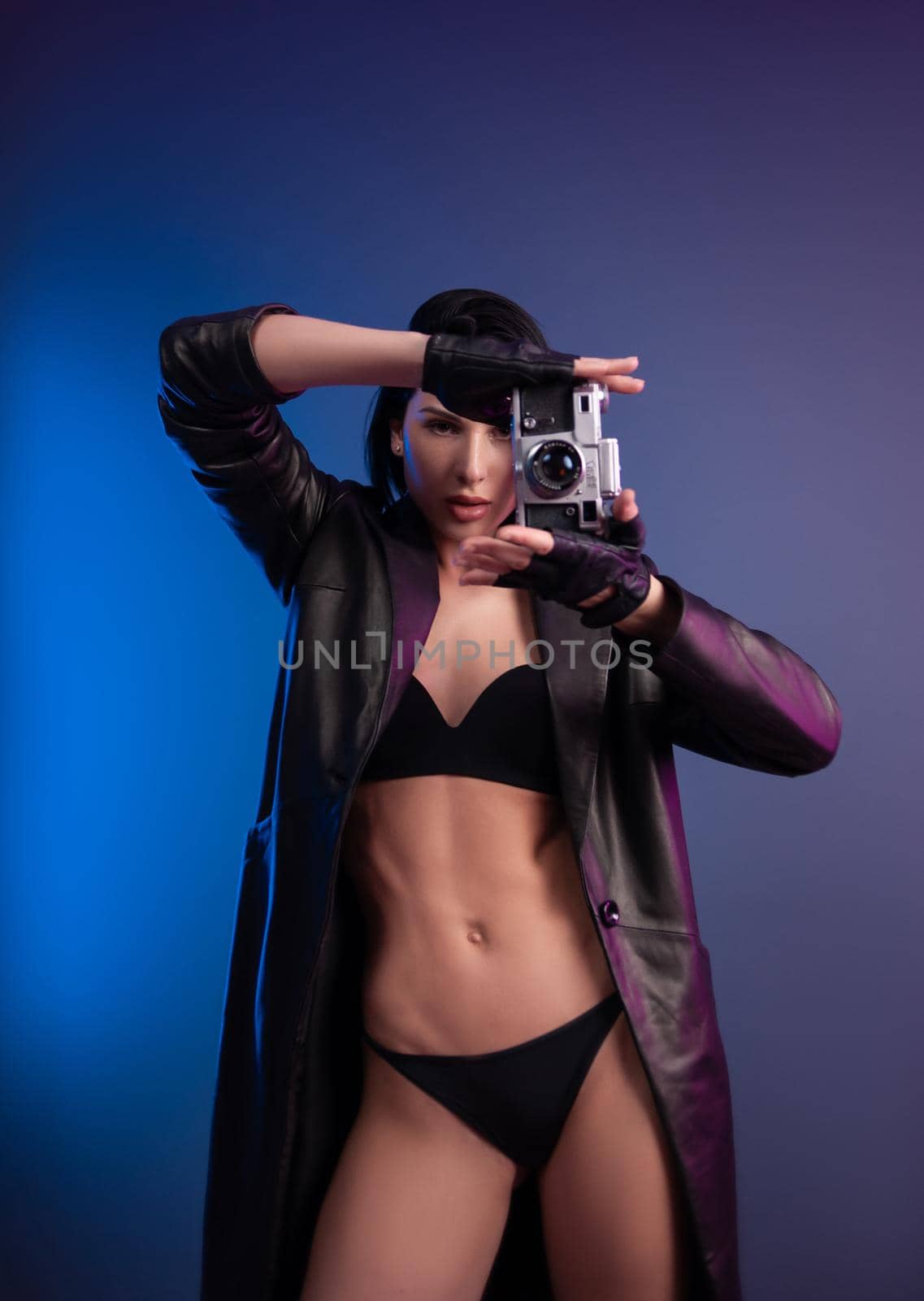 the brunette photographer girl in underwear and a leather raincoat poses in a photo studio with a camera