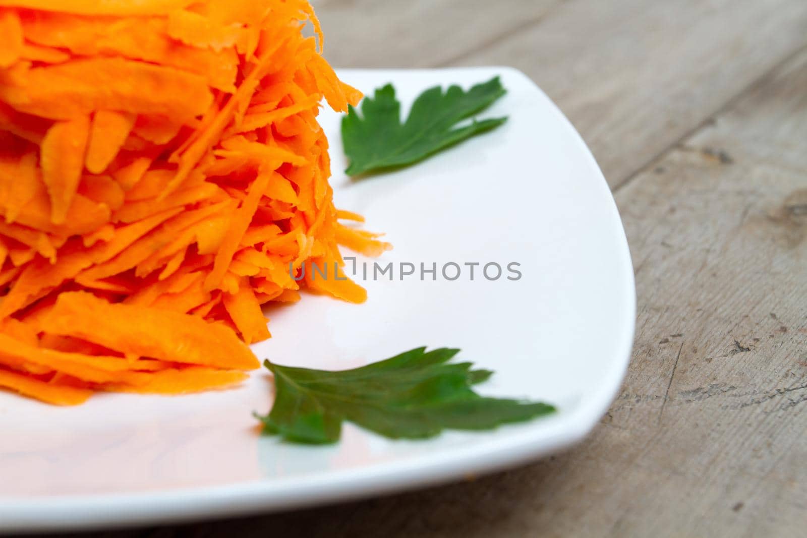 Grated carrot with parsley on a white plate, close-up