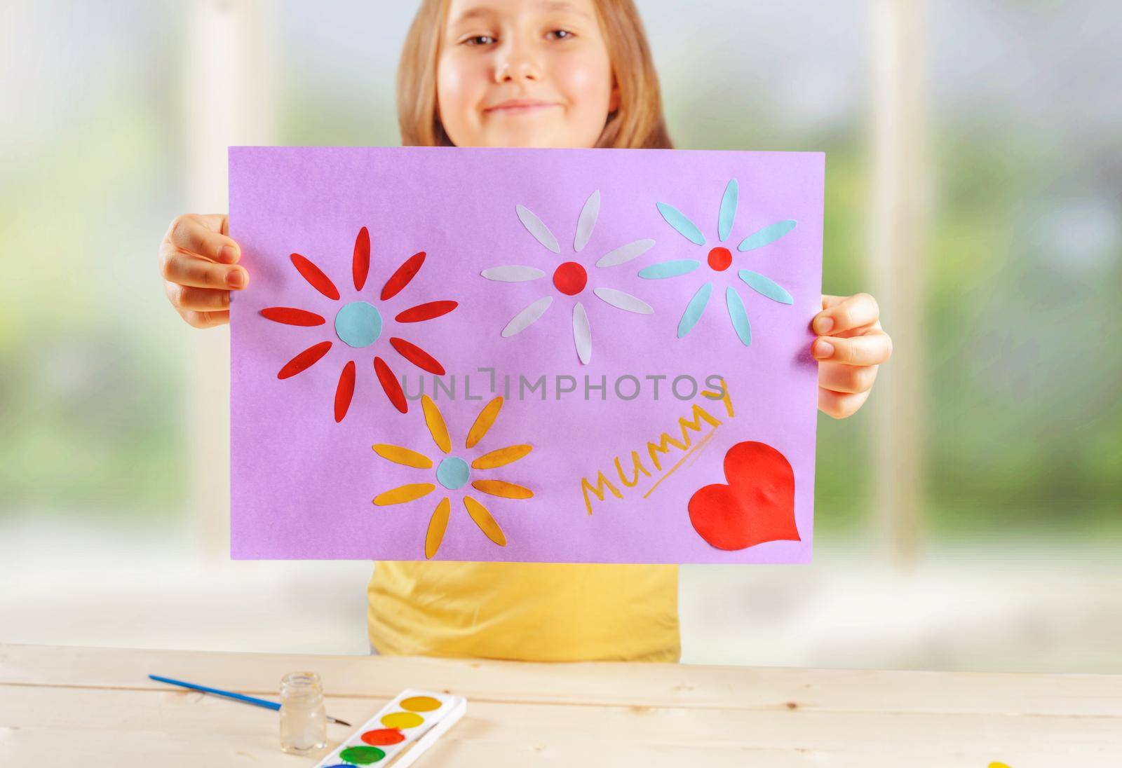 Happy little girl is showing greeting card for mothers day, focus on card