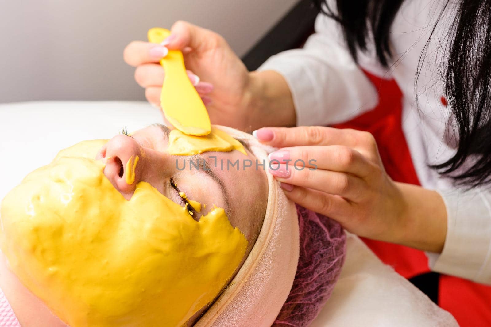Moisturizing the skin at the spa, the beautician applies a gold mask to the client's face. new