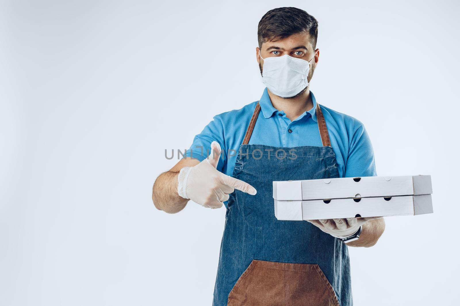 Pizza delivery man in medical gloves and mask against grey background. Safe service while coronavirus covid-19 outbreak